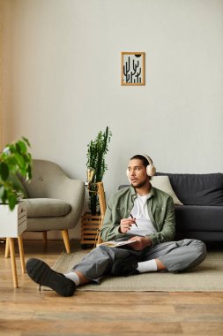 Genç, yakışıklı adam rahat bir şekilde evinde oturuyor, rahat bir atmosferde kulaklıkla resim çiziyor..