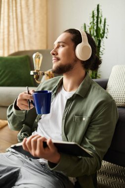 Genç yakışıklı bir adam evde rahatça oturur, kahvesini yudumlar ve yazarken müzik dinler..
