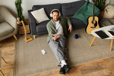 Genç bir adam şık oturma odasında dinleniyor, kulaklıklarla tabletine sarılmış..