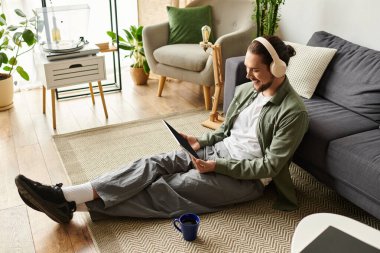 Rahat bir oturma odasında, kulaklıklı genç bir adam tabletine bağlanırken gülümsüyor..