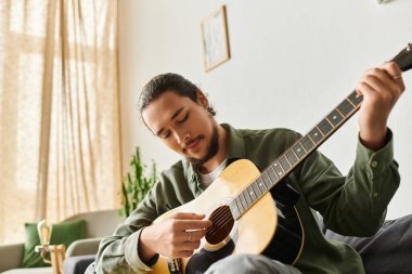 Genç bir adam evde akustik gitar çalıyor, yaratıcılık anının tadını çıkarıyor..