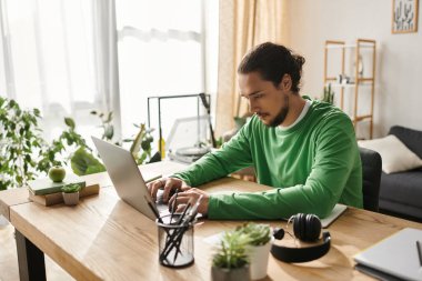Rahat bir ofiste, genç bir adam dizüstü bilgisayarıyla yazar, etrafı bitkilerle çevrilidir..