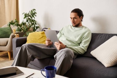 Genç ve yakışıklı bir adam şık bir oturma odasındaki kanepede rahatça oturur ve dikkatle kitap okur..