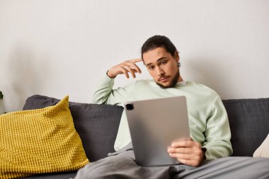 Kanepedeki adam, tabletine odaklanmış, rahat bir iç mekanda rahatlamış..