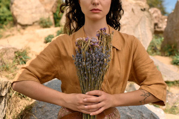 Young woman with curly hair poses outdoors with a bouquet of dried flowers in nature.