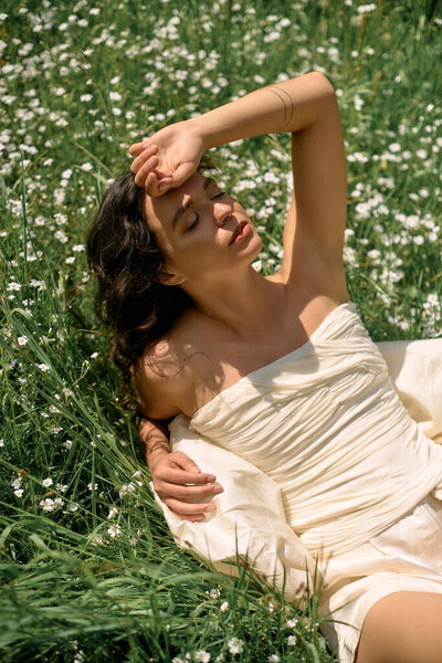 A young woman with curly hair relaxes in a field, enjoying the warmth of summer and bright flowers.