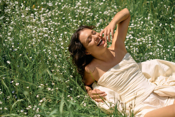 A young woman with curly hair laughs joyfully while lying in a field of flowers on a sunny day.