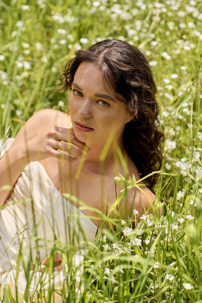A young woman with curly hair poses gracefully in a lush green meadow filled with flowers.