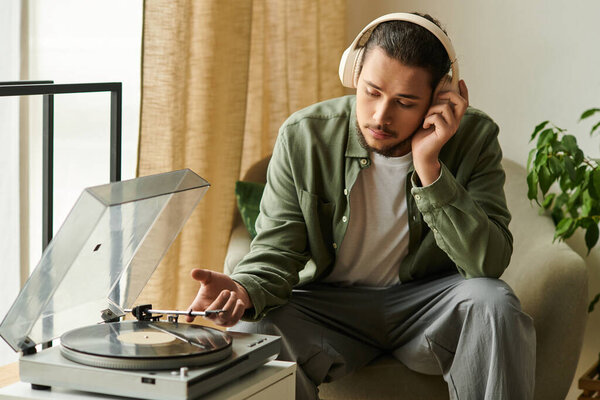 Молодой красивый мужчина слушает музыку, расслабляясь дома, наслаждаясь своими любимыми виниловыми пластинками.