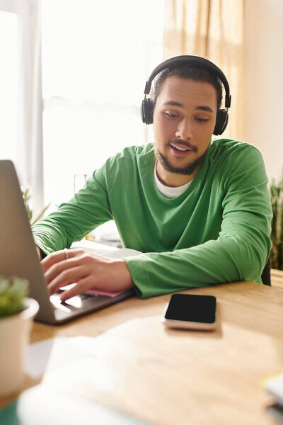 A young handsome man focuses on his laptop, enjoying a productive day at his cozy home workspace.
