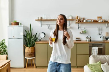 Genç bir kadın sıcak bir içki tutarken gülümsüyor, rahat ve davetkar bir ev ortamı sunuyor..