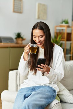 Genç bir kadın sıcak, davetkar bir ev ortamında telefonuyla kayarken çayının tadını çıkarıyor..