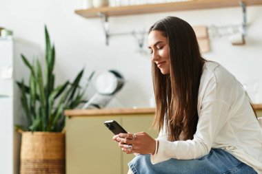 Güzel bir kadın evinde rahat bir şekilde oturur, mutlu bir şekilde akıllı telefonuna odaklanır ve gülümser..