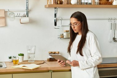 Rahat giysiler içindeki genç bir kadın sıcak bir mutfakta tabletinin tadını çıkarıyor..
