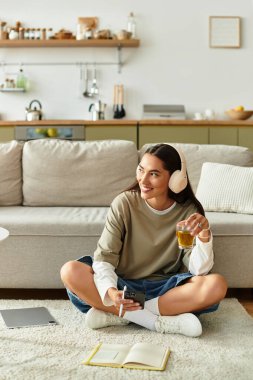 Güzel bir kadın evinde rahat kıyafetler, kulaklıklar ve içkisiyle rahatlar, gülümser..