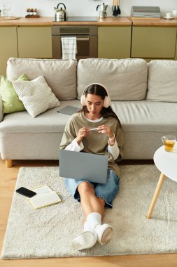 Güzel genç bayan yerde rahatça oturup çayını yudumlarken dizüstü bilgisayarına odaklanıyor..