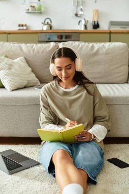 Genç bir kadın günlüğünü yere yazıyor, rahat bir şekilde müzik dinliyor..