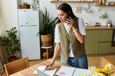 Samimi bir mutfakta genç bir kadın telefonda notlar alırken sohbet ediyor..