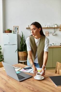 Evde dinlenen genç bir kadın, güneşli bir günde çalışma alanını düzenlerken çayını yudumluyor..