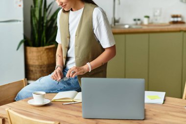 Genç bir kadın rahat evinde rahatlıyor, kahvesini yudumlarken dizüstü bilgisayarına odaklanıyor..