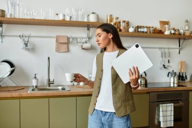 Modern bir mutfak düzeninde laptopuyla çalışırken kahvenin tadını çıkaran güzel bir kadın..