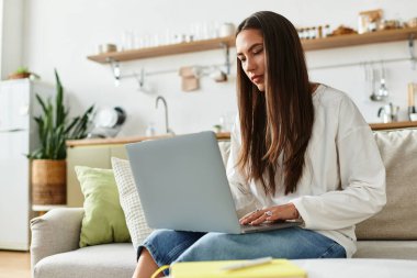 Kanepede dinlenen genç bir kadın dikkatle dizüstü bilgisayarına odaklanarak rahat bir atmosfer yaratıyor..