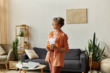 Son sınıf öğrencisi bir kadın oturma odasında huzur içinde durup sıcak bir içeceğin tadını çıkarıyor..