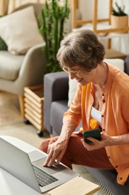 Rahat giyinen olgun bir kadın laptopuyla sıcak, davetkar bir yaşam alanında karşılaşır..