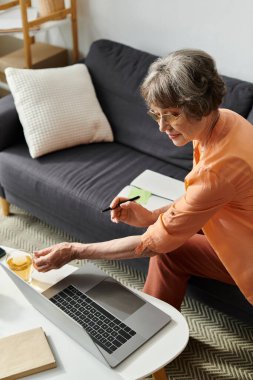 Rahat giyinen yaşlı bir kadın çay içerken internetten iş yapıyor..