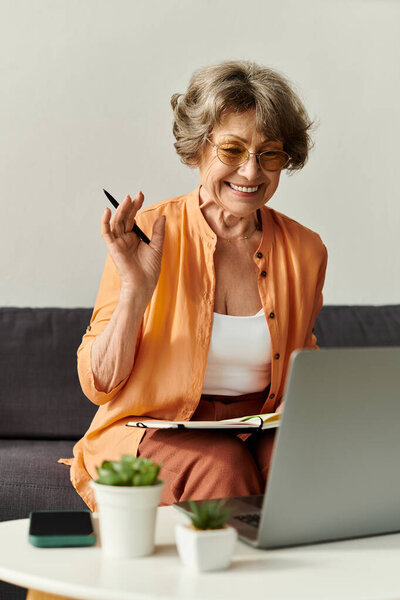 Зрелая женщина в уютной одежде улыбается и машет волнами, участвуя в онлайн-чате дома.