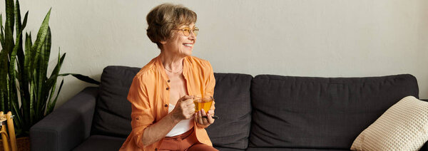 A senior woman smiles warmly while sipping tea in her cozy living room, radiating happiness.