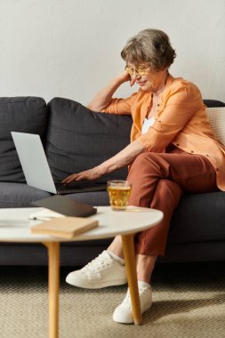 Olgun bir kadın kanepede rahatlar, rahat evinde online aktivitelerle meşgul olur..