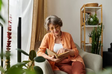 Samimi giyinmiş yaşlı kadın, sakin evinde bitkilerle çevrili bir kitap okuyor..