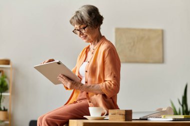Rahat giyimli olgun bir kadın evde rahatça dinlenirken tablet kullanır..
