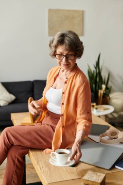 Rahat bir şekilde giyinen son sınıf öğrencisi evde rahatlıyor ve bir fincan sıcak kahvenin tadını çıkarıyor..