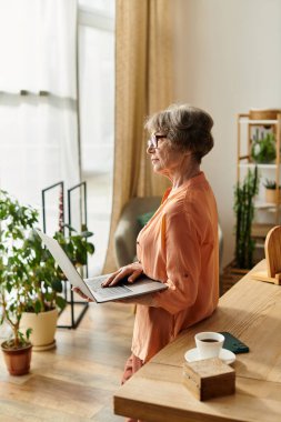 Huzurlu bir ev ortamında, son sınıf öğrencisi bir kadın dizüstü bilgisayarıyla durup rahatlığı ve sakinliği kucaklıyor..