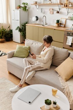 Rahat giysiler içinde olgun bir kadın koltuğa oturur ve telefonuna odaklanır..