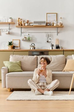 Yaşlı kadın rahatça yerde oturuyor, içkisinin tadını çıkarıyor ve sıcak atmosferin tadını çıkarıyor..