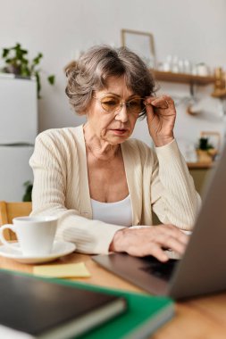 Sıcak ve davetkar bir mekanda, olgun bir kadın dizüstü bilgisayarına sarılıp çayını yudumluyor..