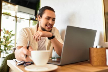 Sakallı genç adam yaz boyunca canlı bir kafede kahvesini yudumlarken dizüstü bilgisayarına odaklanıyor..