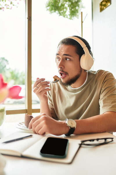 A young man with a beard savors cake and drink in a cafe.