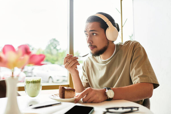 Focused man savors cake and matcha while sitting in cafe with headphones on.