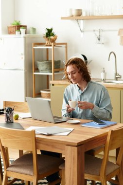 Rahat genç adam ev ortamında laptopuyla uğraşırken kahvesini yudumluyor..