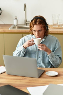 Yakışıklı genç adam evde uzaktan çalışmakla meşgulken düşünceli bir şekilde kahvesini yudumluyor..