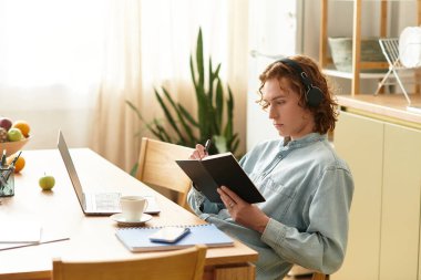 Defterine odaklanmış genç bir adam, parlak bir ev ortamında yaratıcı bir anın tadını çıkarıyor..