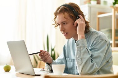 Evde işe dalmış, bilgisayarı ve kulaklığı kullanan yakışıklı bir genç..