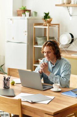Genç bir adam yemek masasında oturur, rahat bir mutfakta kahvesini yudumlarken dizüstü bilgisayarına odaklanır..