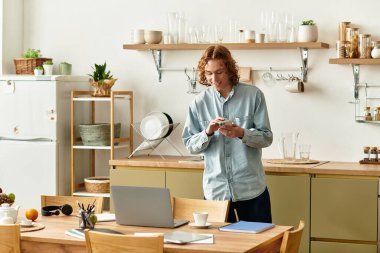 Yakışıklı genç adam rahat bir mutfakta duruyor, rahat bir anda akıllı telefonuyla meşgul oluyor..