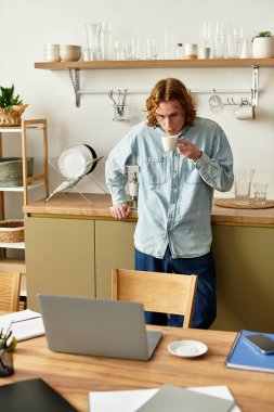 Genç adam modern ev ofisinde sıcak bir fincan kahveye bayılıyor, düşüncelere dalmış..