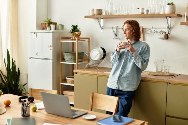 Evde dinlenen yakışıklı genç bir adam, etrafı temiz bir mutfakla çevriliyken kahvesinin tadını çıkarıyor..